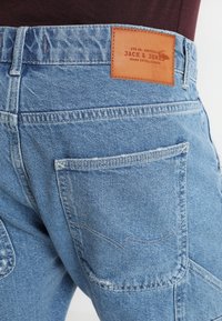 Ljusblå denimjeans med en läderlapp med "Jack & Jones" på baksidan, flera fickor och en strukturerad yta.