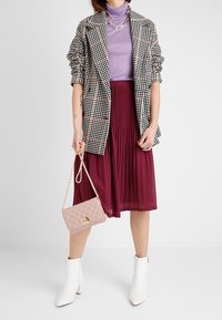 Blazer in bianco e nero a motivo houndstooth, dolcevita viola, gonna plissettata bordeaux, stivali alla caviglia bianchi e una borsa rosa trapuntata con manico a catena.