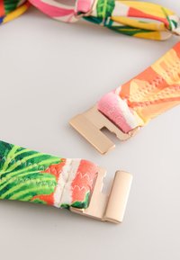 Fermeture métallique avec des sangles en tissu aux motifs colorés de feuilles tropicales et florales, présentée ouverte sur une surface unie.