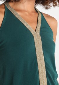 Turkos ärmlös topp med en glittrande gyllene kant längs halsringningen, med en mjuk, smidig textur och en avslappnad design.