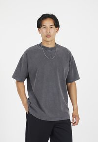 Grå överstor T-shirt i bomull med korta ärmar, rundad halsringning och avslappnad passform. Slät textur med subtila färgvariationer.