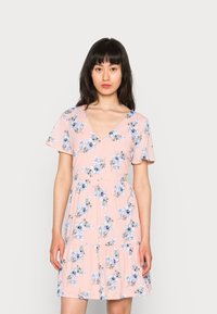 O vestido floral rosa tem mangas curtas, um decote em V e uma bainha em camadas. Feito de um tecido leve com padrões de flores azuis.