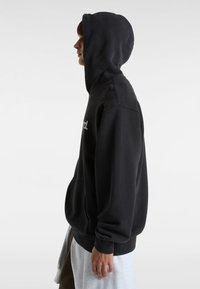 Sort hættebluse med ribbede manchetter og kant, prydet med en frontlomme og en hætte med snoretræk. Materialet ser blødt og fleece-lignende ud.