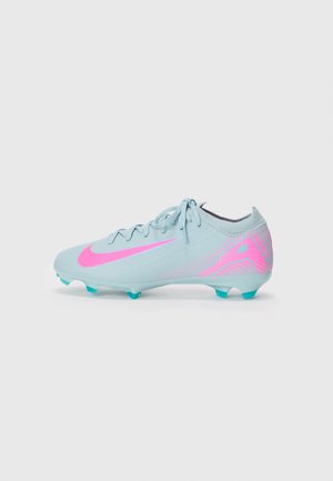 Botas de fútbol azul claro con el logo de Nike rosa y diseño, tacos azul verdoso y cordones sobre un fondo blanco liso.