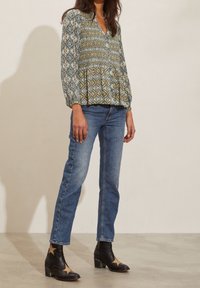 Långärmad blus i teal, guld och krämfärgad geometrisk mönster, ihop med blå denimjeans och svarta ankelstövlar med gulddetaljer i form av stjärnor.