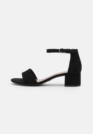 Black suede ankle strap sandal with a wide front band, low block heel, and a buckle closure, featuring a smooth texture and open toe design.