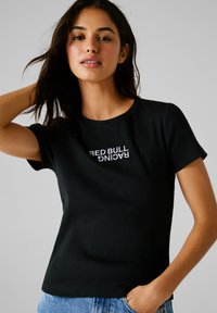 Schwarzes, geripptes T-Shirt mit Rundhalsausschnitt und kurzen Ärmeln, das auf der Vorderseite den gestickten Text "RED BULL RACING" in Weiß trägt.