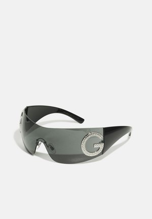 Óculos de sol pretos com um design elegante, lentes cinza fumê, apresentando um grande logo "G" decorado com strass de um lado.