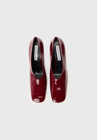 Pantofi cu toc din piele lacuită burgundă, cu vârf pătrat, textură netedă și decupaj jos pentru un design elegant. Eticheta este vizibilă în interior.