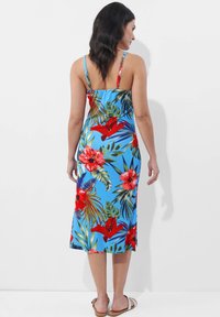 Blumige Midi-Kleid in Blau mit roten Hibiskus- und grünen Blättermustern. Mit dünnen Trägern und einer taillierten Silhouette. Glatte Stofftextur.