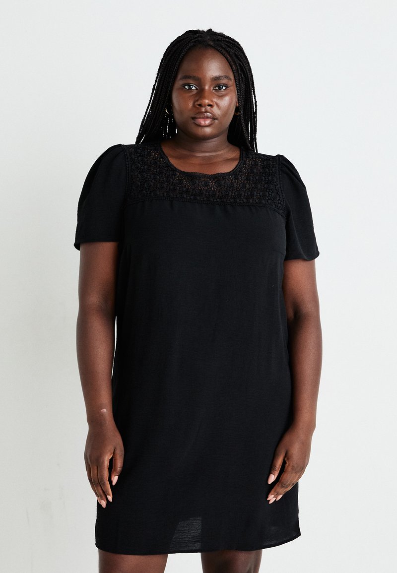 Robe en coton noir avec des manches courtes, un empiècement en dentelle texturée et une coupe décontractée qui arrive au milieu de la cuisse. Fini lisse et mat.