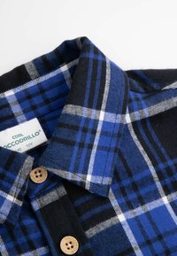 Niebieska i czarna koszula w kratę z kołnierzykiem, z zapięciem na guzik, wykonana z miękkiego materiału z białymi i szarymi liniami krzyżującymi się w wzór kratki.