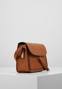 Brun läderhandväska med klaffstängning, guldfärgad metall, detalj med tofs och kontrasterande svart sömnad. Strukturerad form.