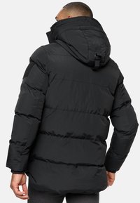 Geacă puffer neagră cu un design căptușit, glugă atașată și curea ajustabilă. Prezintă un finisaj texturat și accente de cusătură vizibile.