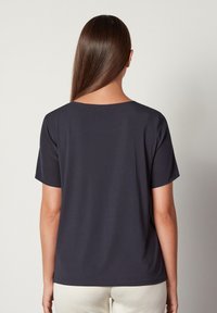 Marineblå kortærmet t-shirt med bred halsudskæring, glat stof og afslappet pasform, vist fra ryggen mod en neutral baggrund.