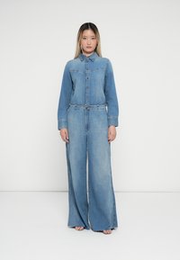 Denim jumpsuit featuring a button-up front, long sleeves, and wide legs. Light blue wash with stitching details and elastic waistline.