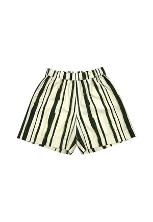 Donna in piedi con le mani in tasca, indossa una maglietta verde oliva, pantaloncini bianchi con righe verticali verdi e scarpe da ginnastica multicolori.