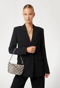 Blazer noir ajusté avec des revers, associé à un sac à main en satin matelassé gris doté d'une chaîne en argent et d'accents décoratifs.