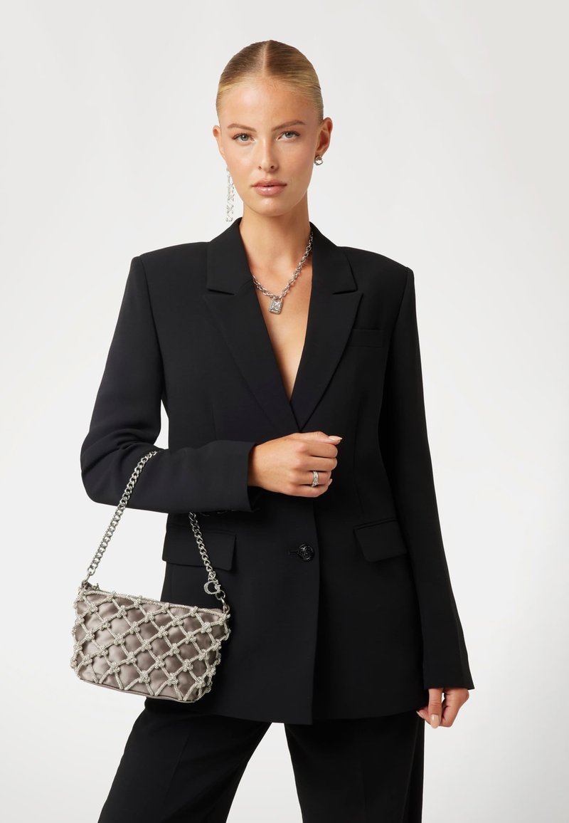 Blazer noir ajusté avec des revers, associé à un sac à main en satin matelassé gris doté d'une chaîne en argent et d'accents décoratifs.