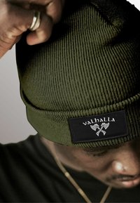 Green ribbed knit beanie with a black label displaying the word "valhalla" and crossed axes, showcasing a textured finish.