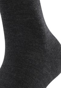 Tmavě šedá ponožka vyrobená z měkké, mírně strukturované tkaniny. Má žebrovaný vzor a hladké kontury, vhodná pro běžné nošení.