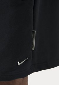 Calções Nike em algodão preto liso, com um logo branco e um rótulo que diz "NIKE STANDARD ISSUE." Textura suave, ajuste padrão.