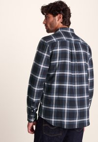 Navy and grey plaid flannel shirt with long sleeves, buttoned cuffs, and a back yoke detail, featuring a softly textured fabric.