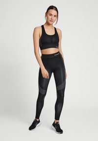 Svart sportbh och högmidjade leggings, tillverkade av stretchigt material med reflekterande detaljer och geometriska mönster, kombinerat med svarta sneakers.