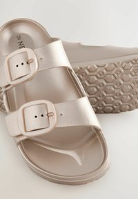 Sandali a doppia cinghia in oro rosa metallico con fibbie regolabili. Suola a nido d'ape testurizzata per aderenza e supporto. Finitura liscia sulle cinghie.