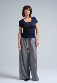 Tamsiai mėlyna prigludusi t-shirt su apvalia iškirpte, derinama su laisvais šviesiai pilkais plačiais kelnais su raišteliu. Lygi tekstūra. Juodi batai.