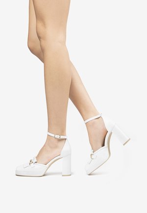 Białe szpilki na platformie, z kwadratowym noskiem, paskiem na kostkę i złotymi akcentami. Gładka skórzana faktura.