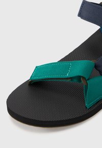 Vihreät ja tummansiniset säädettävät hihnasandaalit, joissa on teksturoitu musta pohja ja sileä beige pohja, joissa on mukava litteä muotoilu.
