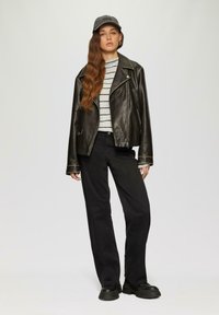 Zwarte leren motorjack over een grijs-wit gestreept sweater, gecombineerd met zwarte wijde broek en chunky zwarte schoenen. Een pet maakt de look compleet.