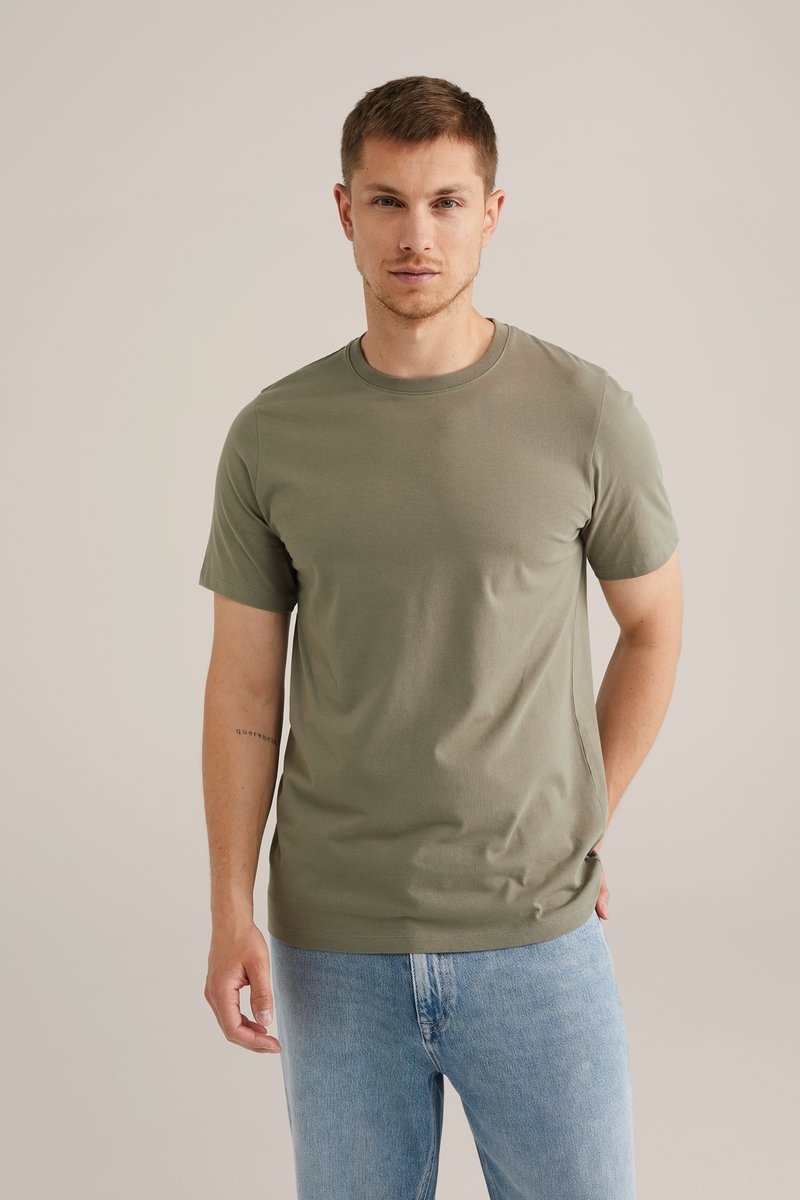 Camiseta de manga corta en verde oliva hecha de algodón suave, con un cuello redondo clásico y un ajuste relajado, combinada con jeans azul claro.