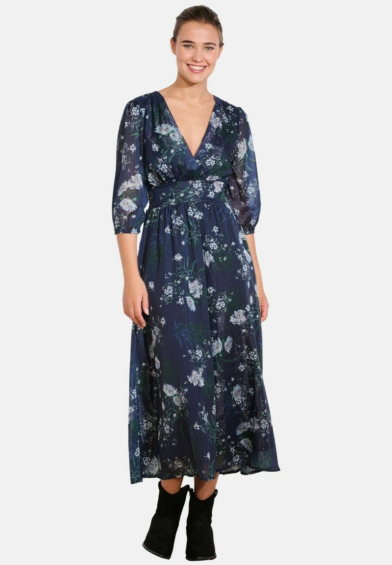 Blumen-Maxi-Kleid mit tiefem V-Ausschnitt, 3/4 durchsichtigen Ärmeln, tailliertem Schnitt und einem navyfarbenen Grundton, der mit weißen und grünen Blumenmustern versehen ist.