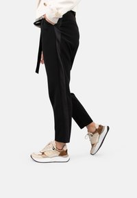 Pantalons noirs à coupe slim avec une bande latérale en satin, associés à des baskets beiges et brunes avec des panneaux texturés et une semelle rembourrée.