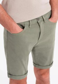 Shorts vert kaki à coupe droite, fabriqués en coton texturé, avec des revers, des poches latérales et une fermeture à bouton.