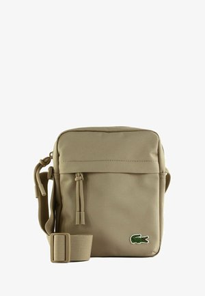 Borsa a tracolla beige con tracolla regolabile, tasca frontale con zip e piccolo logo di coccodrillo verde nell'angolo in basso a destra.