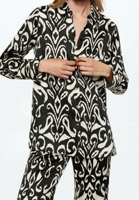 Camicia a maniche lunghe a righe bianche e nere, con chiusura a bottoni e colletto classico, abbinata a pantaloni a righe coordinate.