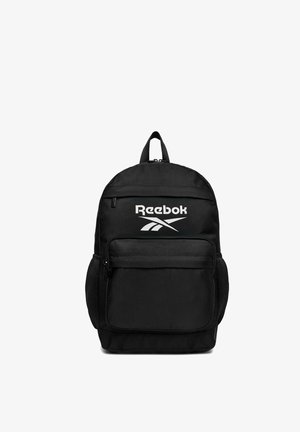 Mochila negra de Reebok con logo blanco, bolsillo frontal con cremallera, bolsillos laterales de malla y asa superior para transportar sobre un fondo blanco.