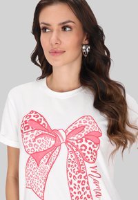 Hvid t-shirt med et stort pink leopardmønstret sløjfegrafik. Designet har detaljer i mørkere pink og inkluderer teksten "Mama."