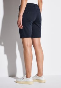 Pantalones cortos de algodón azul marino con bolsillos, que presentan una textura suave y un corte recto. Combinados con zapatillas blancas, con marca visible en los zapatos.