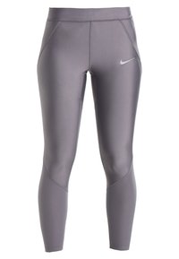 Szare legginsy sportowe z gładkiego, elastycznego materiału. Zawierają logo Nike oraz siateczkowe akcenty przy kostce, zapewniające wentylację.