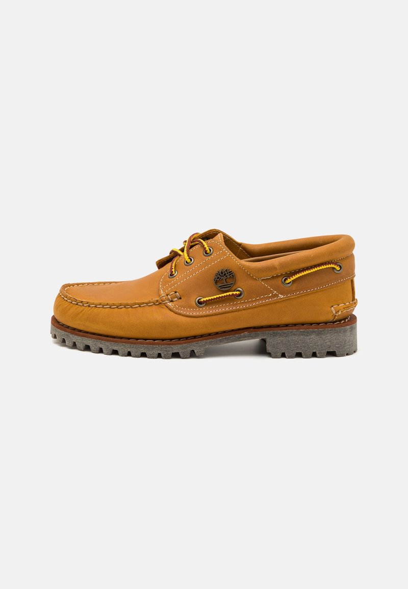 Chaussure bateau en cuir marron clair avec lacets jaunes et marron, couture moc toe, col rembourré et semelle grise robuste.