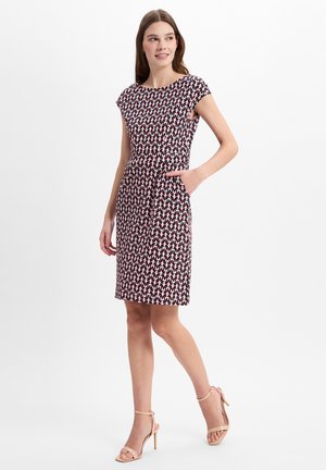 Kleid mit Cap-Ärmeln in einem schwarz-weißen Blumenmuster mit pinken Akzenten, tailliertem Schnitt und Taschen. Getragen mit beigen Riemchen-Heels.