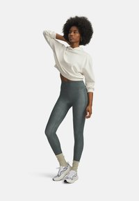 Cropped white sweatshirt, high-waisted dark green leggings with side seams, and grey-and-white sneakers with textured socks.