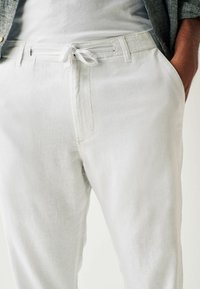 Pantalons en lin gris clair avec un cordon de serrage, présentant une coupe décontractée et une texture lisse, montrant uniquement la taille et les hanches.