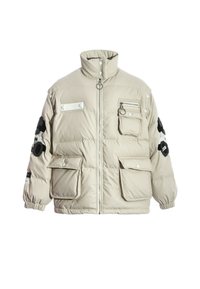 Chaqueta acolchada beige con cuello alto, cierre frontal, múltiples bolsillos y detalles bordados en negro texturizado en las mangas.