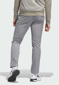Pantalons de sport gris en matériau léger, avec une coupe slim et une ceinture élastique, associés à des sneakers et des chaussettes blanches.