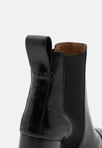 Bottine en cuir noir avec panneau latéral élastique et languette en relief portant le logo « See by Chloé », doublure intérieure beige et talon superposé.